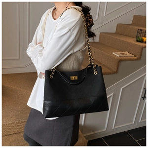 Detail of black quilted tote bag with gold chain strap and square metal twist lock