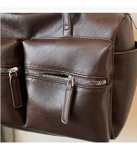 Detail of dark brown leather underarm bag featuring dual front pockets and silver zippers