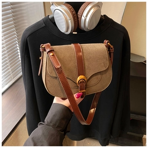 Detail view of brown suede saddle bag with leather flap and vintage gold buckle hardware