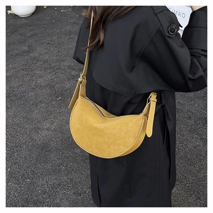 Close-up of yellow leather crescent bag with wide shoulder strap worn on black coat