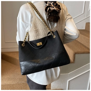 Detail view of a large black quilted tote bag with gold chain strap and metal turn-lock
