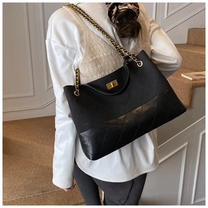 Model wearing a large black quilted tote bag with golden chain straps on a staircase