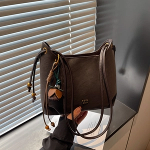 Detail of a dark brown crossbody bag with drawstring strap and flower pendant