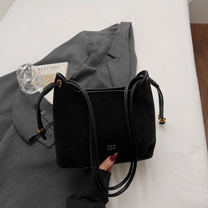 Detail of matte black suede shoulder bag with gold logo and metallic hardware