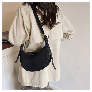 Detail of a black matte crescent bag with adjustable strap and golden hardware on a model