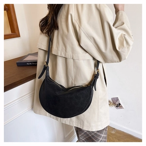 Detailed view of black crescent crossbody bag worn over a beige coat with gold hardware