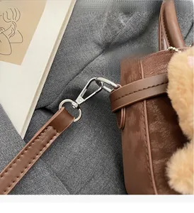 Détail du crochet métallique argenté sur sac bandoulière en daim brun avec breloque