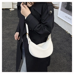 Close-up of a white leather dumpling bag with adjustable strap on a black coat