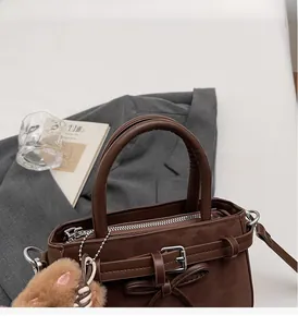 Détail d'un sac à main marron café en daim avec un nœud et un pendentif en peluche