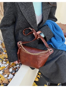 Détail du sac bandoulière demi-lune caramel avec chaîne dorée sur un manteau gris