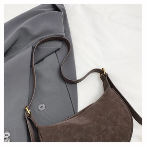 Detail of dark brown suede crescent bag with adjustable strap and gold metal buckle