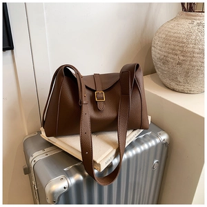 Détail d'un sac cabas en cuir grainé marron foncé avec boucle dorée sur une valise argent