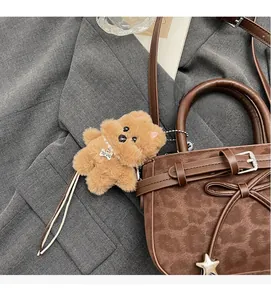 Détail d'un pendentif chien en peluche marron avec collier perlé sur un sac en cuir mat