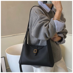 Détail du sac sous le bras en cuir grainé noir avec boucle dorée porté par mannequin