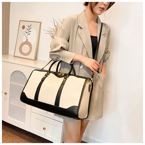 Detail of a canvas travel tote bag with black leather trim and gold hardware accents