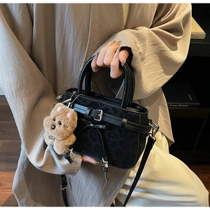 Détail du sac à main noir gaufré léopard avec nœud en ruban et breloque ours
