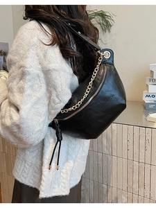 Détail du sac demi-lune noir en cuir avec chaîne dorée et franges sur pull blanc