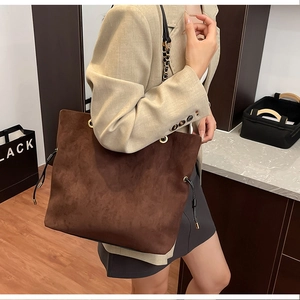 Detail of a large brown suede tote bag with drawstring and chain strap on a model