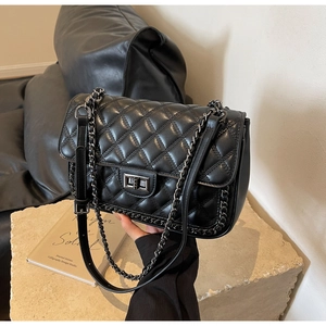 Detail of black quilted leather shoulder bag with silver chain strap and square lock