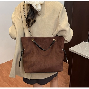 Detail of large brown tote bag with gold chain strap and drawstring on khaki blazer