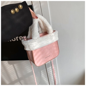 Detail of pink faux fur trim on suede bucket bag held by model in black blazer