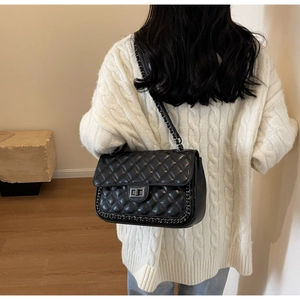 Detail of a black quilted chain bag paired with a white textured cable knit sweater