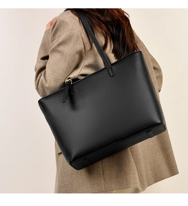 Detail of black pebbled leather tote bag featuring sleek shoulder straps and metallic hardware
