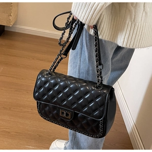 Detail of black quilted chain bag with metallic buckle worn by a model in casual outfit