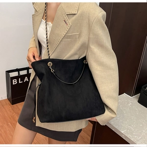 Detail of large black suede tote bag with gold chain strap worn with a beige blazer