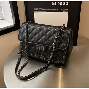 Detail of black quilted leather shoulder bag featuring metal chain and silver twist lock