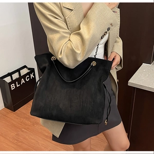 Detail view of black suede tote bag featuring side drawstrings and metal chain strap