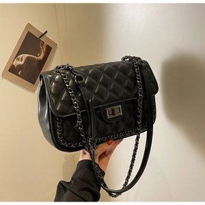 Detail of black quilted leather shoulder bag with dark metal chain strap and turn-lock