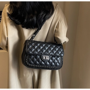 Detail of black quilted leather chain bag with metal lock clasp on khaki trench coat