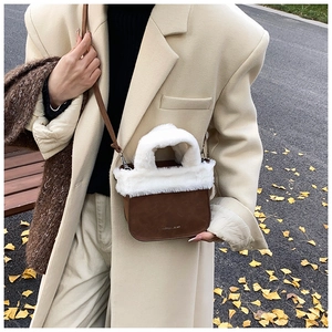 Detailed close-up of brown suede bucket bag with white faux fur trim and metal logo
