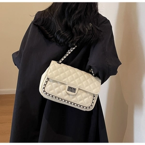 Detail of white quilted chain shoulder bag with metal lock shown on a black coat