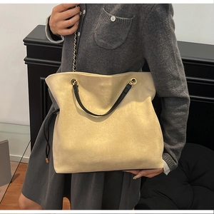 Detail of minimalist beige drawstring tote bag with gold chain strap on model