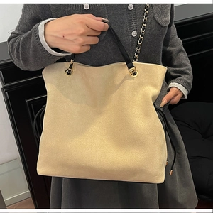 Detail of beige suede drawstring tote bag with black leather handle and gold chain strap