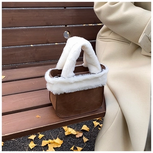 Detail of suede winter bucket bag with white plush trim on a park bench with autumn leaves