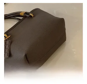 Detail of dark brown tote bag featuring textured grain leather and chocolate charm accessory