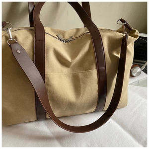Detail of khaki canvas travel tote featuring dark brown leather handles and silver hardware
