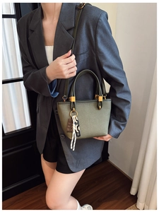 Olive green bucket bag with gold hardware and chocolate charm worn by a model