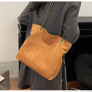 Detail of tan suede tote bag featuring metallic eyelets and leather chain shoulder strap