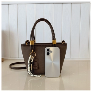Detail view of mini dark brown handbag with woven strap next to a phone for scale