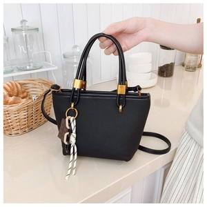 Detail of black trapezoid tote bag with gold hardware and chocolate charm on a counter