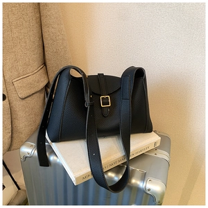 Sac bandoulière en cuir grainé noir avec boucle dorée posé sur une valise argentée