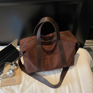 Grand sac cabas en daim marron foncé avec anses en cuir et accessoires de voyage sur fond blanc