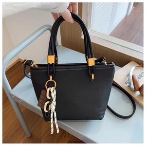 Detail of a black textured tote bag featuring golden hardware and decorative charms