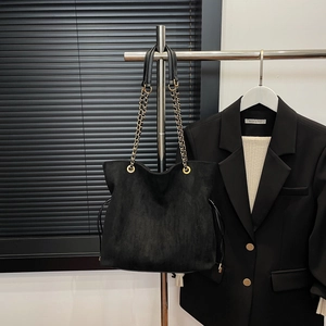 Detail view of large black suede tote bag with gold chain strap and drawstring design