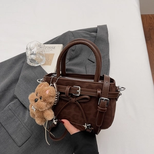Sac à main en daim chocolat avec nœud et breloque ours sur une veste de costume grise