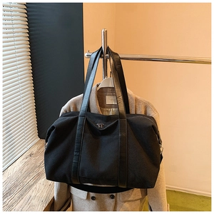Detail of black canvas travel bag featuring long leather handles and top metal zipper
